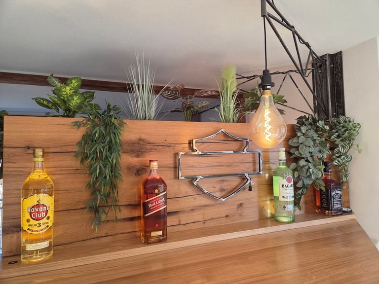 Maßgefertigtes Regal- und Bartresen-Element aus Massivholz mit Flaschenablage, Pflanzen und Industrial-Hängelampe.