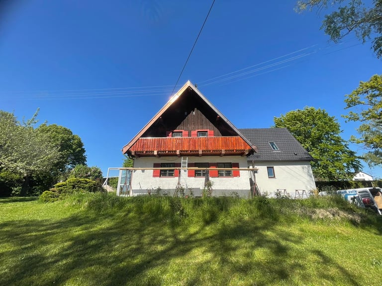 Giebelansicht eines Wohnhauses mit neuem Holzbalkon und roten Fensterläden von Holztechnik Volk am Ammersee