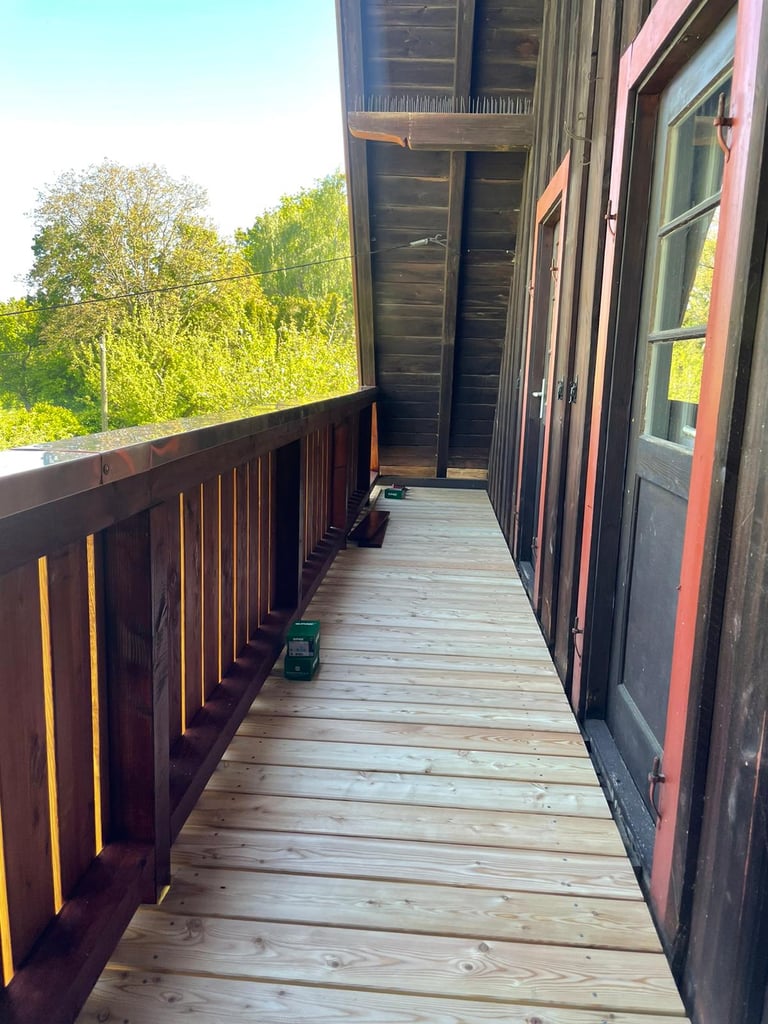 Neu verlegter Balkonboden aus hellen Holz-Dielen auf einem sanierten Holzbalkon mit dunklem Geländer.