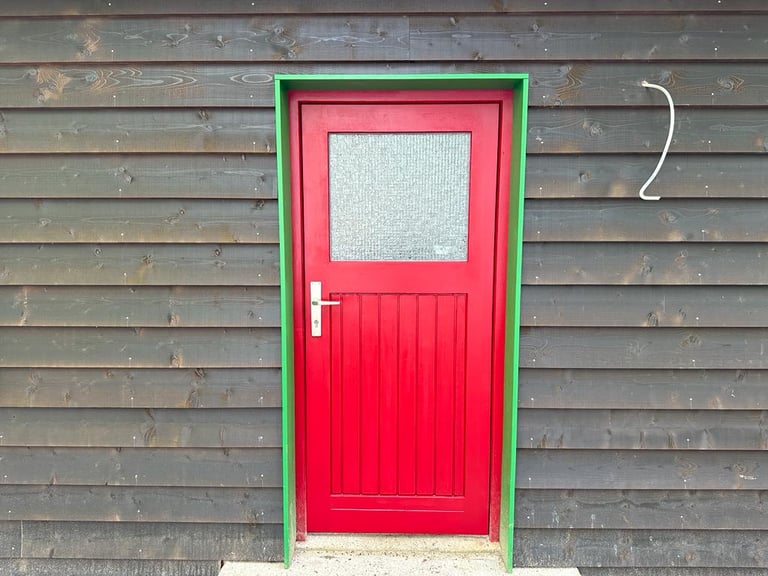 Rot lackierte Holztür mit Strukturglas und grünem Rahmen in dunkler Holzfassade.