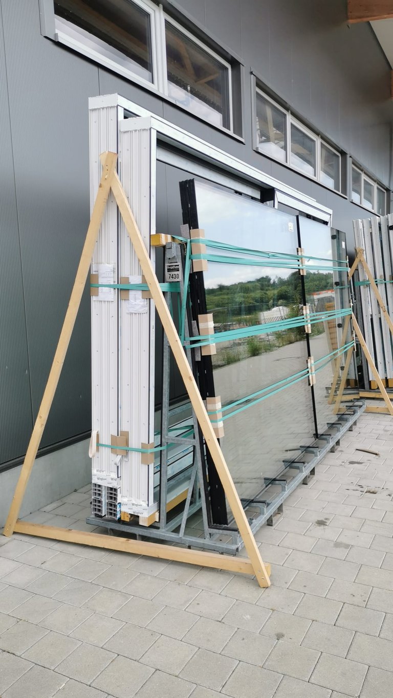 Angelieferte Fenster- und Türelemente sowie große Glasscheiben auf Transportgestellen vor Werkhalle
