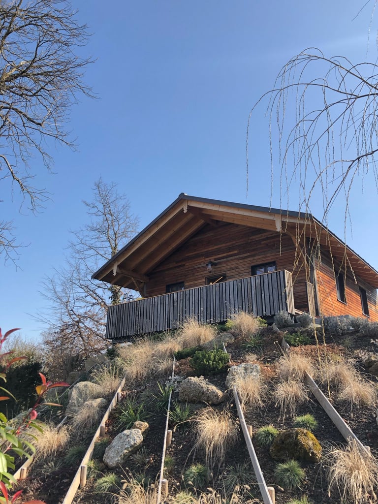 Holzhaus in Hanglage mit Holzfassade und Balkon über dem Garten von Holztechnik Volk am Ammersee
