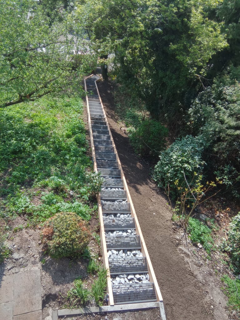 Lange Hangtreppe mit Metall-Gitterroststufen und Holzrahmen durch einen Gartenhang – Holztechnik Volk, Schreiner am Ammersee.