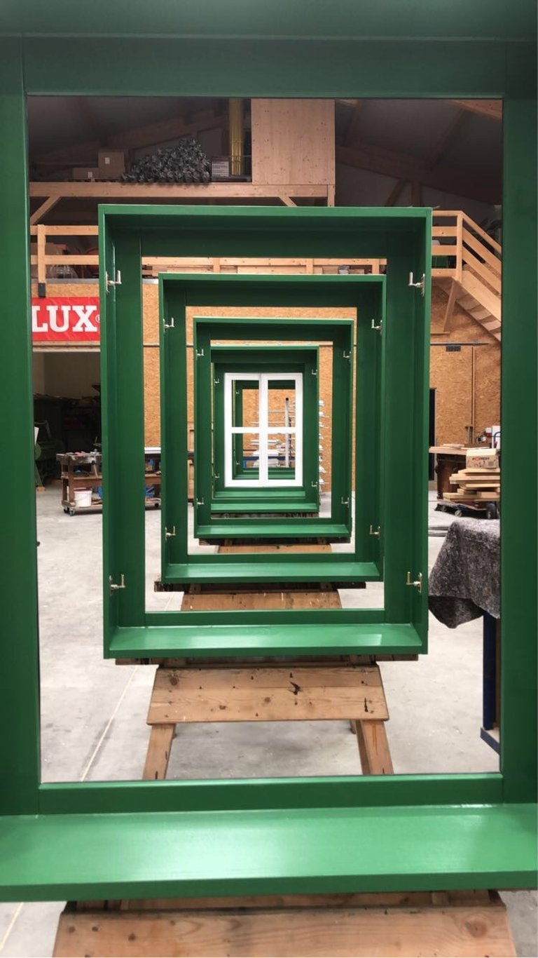 Mehrere grün lackierte Holzfensterrahmen in Reihe auf Werkbank in der Schreinerei.