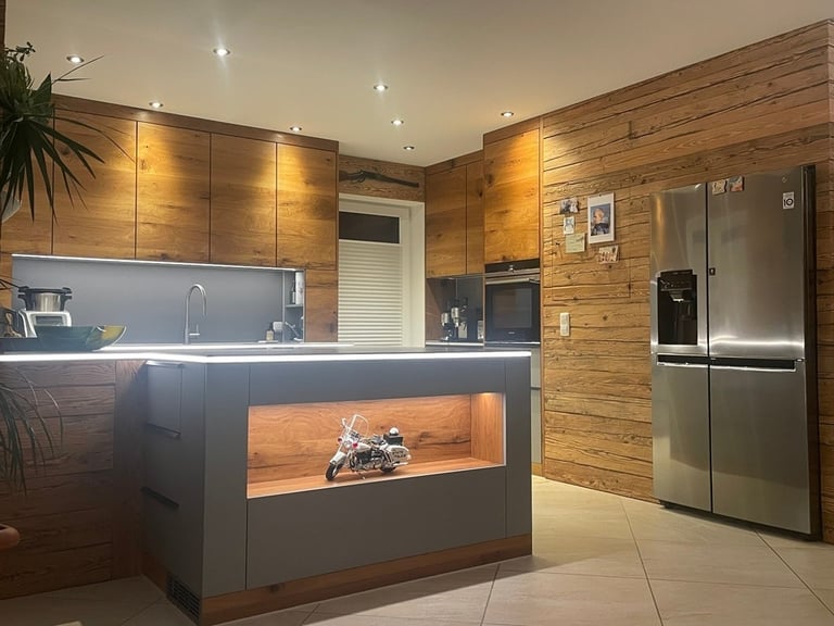 Moderne Küche mit rustikaler Holzverkleidung, grauer Kochinsel mit beleuchteter Nische und großem Edelstahl-Kühlschrank.