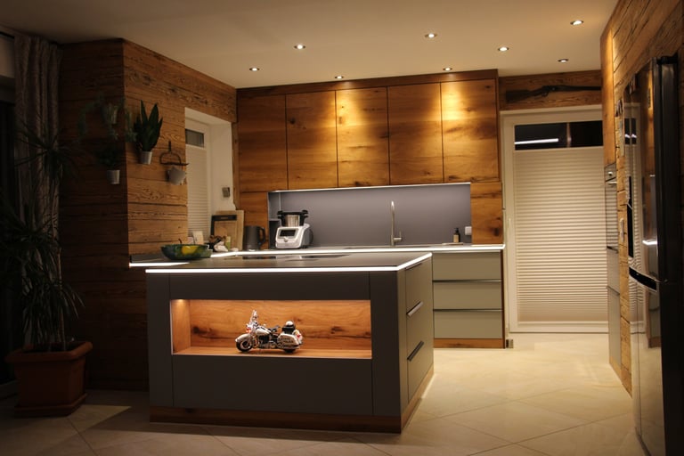 Moderne Küche mit rustikalen Holzfronten, grauer Kochinsel und beleuchteter Nische mit Motorrad-Modell.