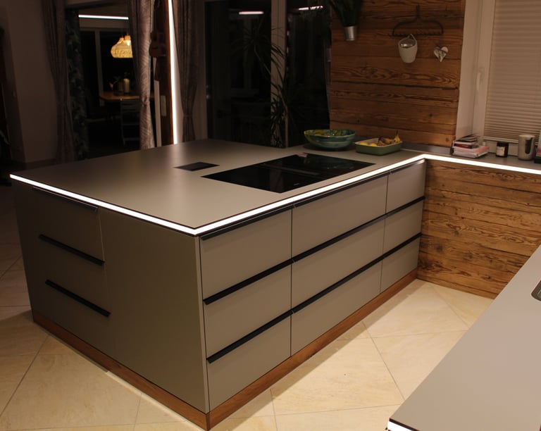 Freistehende graue Kücheninsel mit LED-Beleuchtung, Induktionsherd und Holzsockel vor rustikaler Wandverkleidung.