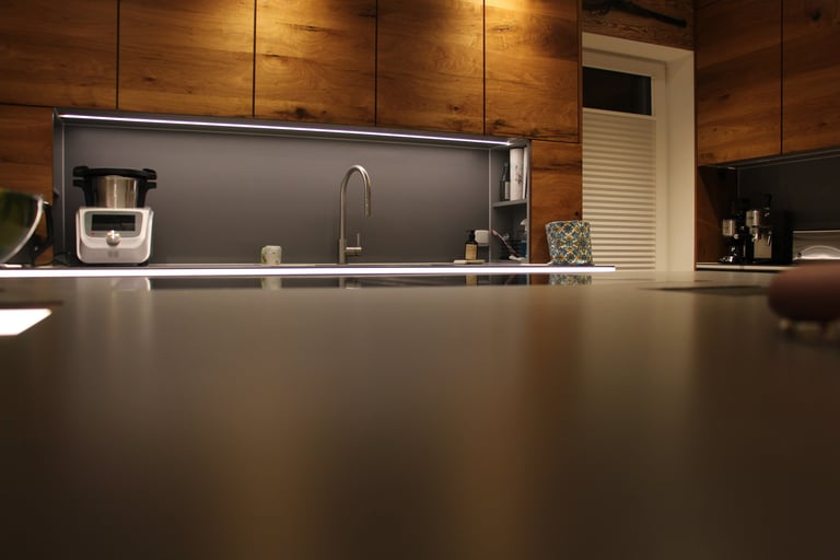 Moderne Einbauküche mit markanten Holzfronten, beleuchteter grauer Nische, Kücheninsel und hochwertigen Geräten.