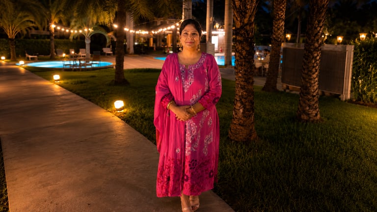 A woman in a pink embroidered Indian kurti posing at a luxury resort with evening string lights.
