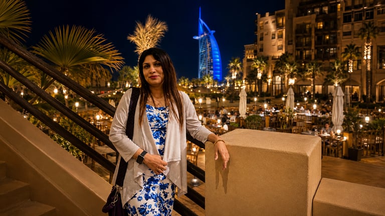 A woman posing at Madinat Jumeirah with the Burj Al Arab hotel illuminated at night in Dubai.