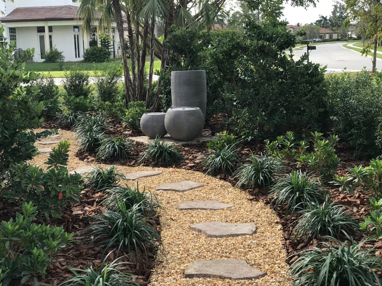 Backyard garden landscaping with a gravel path, stepping stones, and modern stone water fountains.