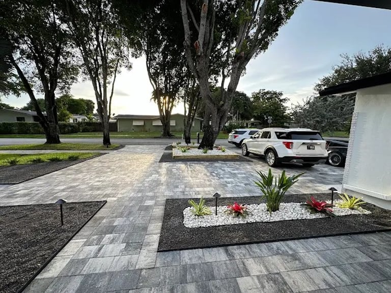Modern driveway featuring grey interlocking pavers, minimalist landscaping with white stones, and outdoor LED lighting.
