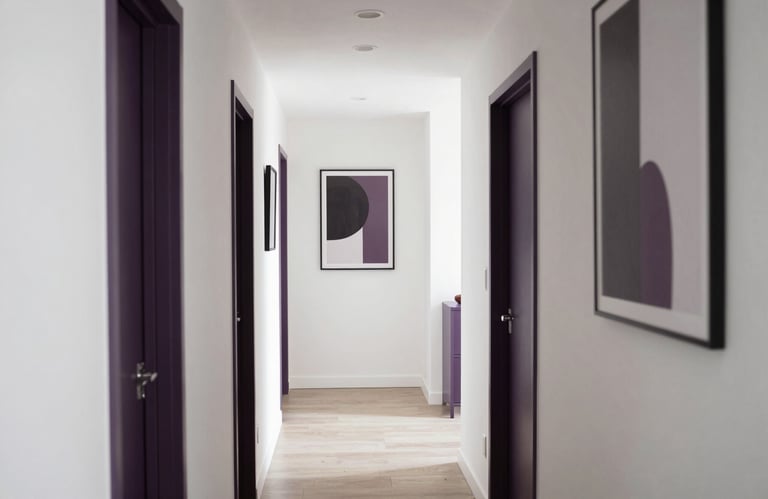 A bright photography shot of a communal hallway or transitional space in a modern home, featuring clean white walls, dark purple accents in the artwork, and soft, natural lighting.