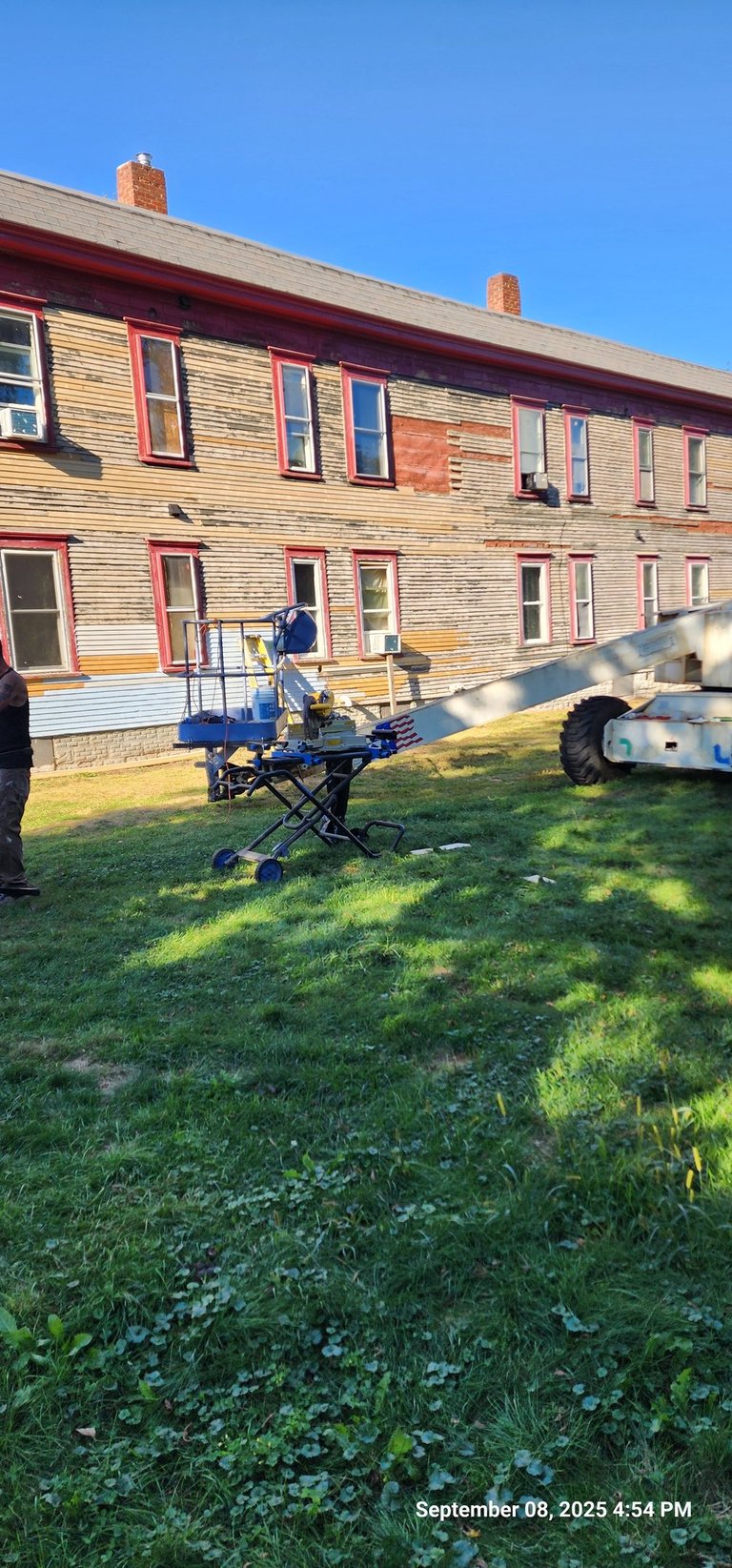 Exterior building restoration using a boom lift for siding repair and painting on an old wooden house.
