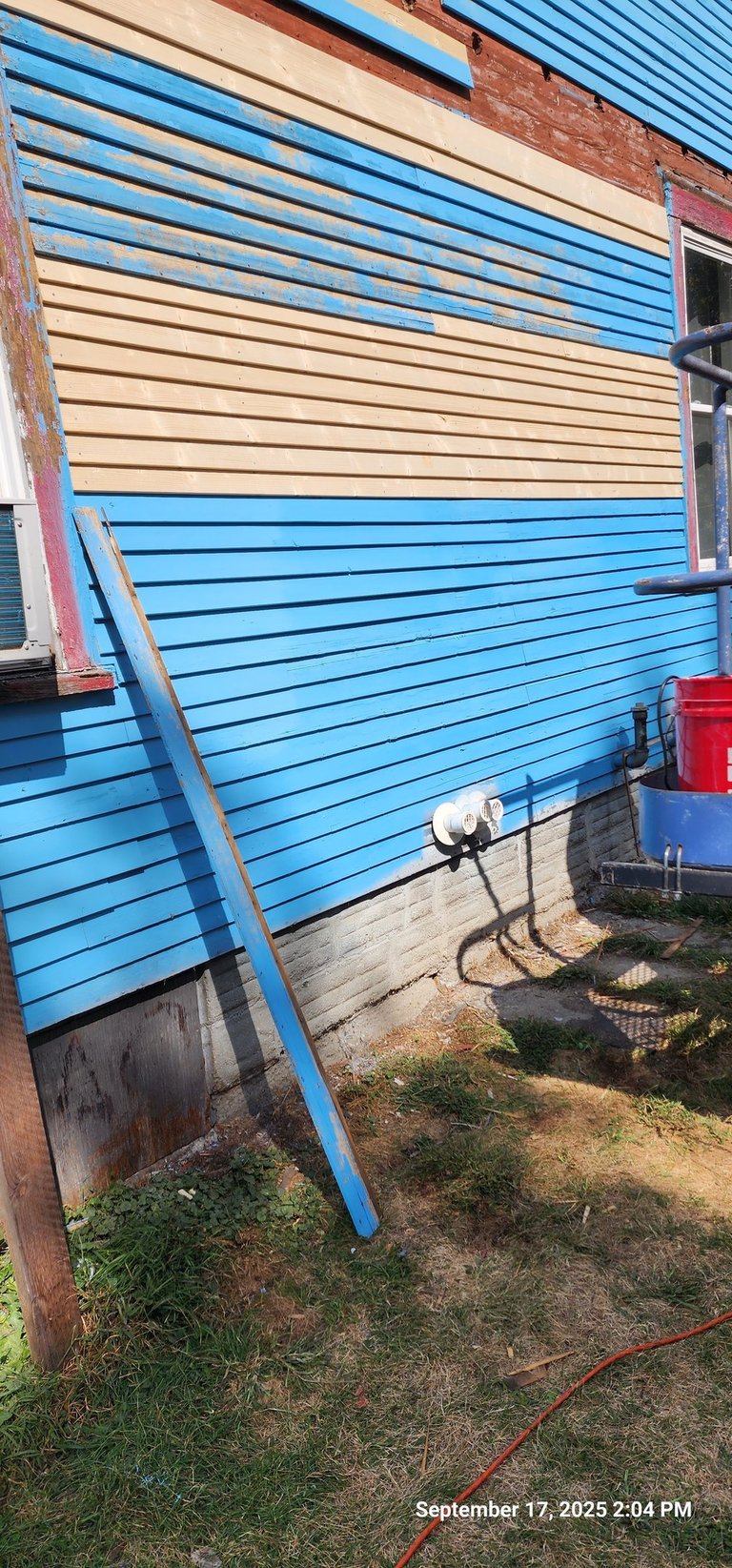 Blue and tan lap siding installation on a residential house exterior with construction tools.