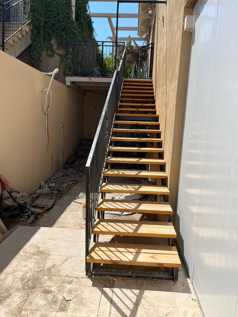Exterior metal staircase with light wood treads leading to a balcony in a sunny outdoor patio space.