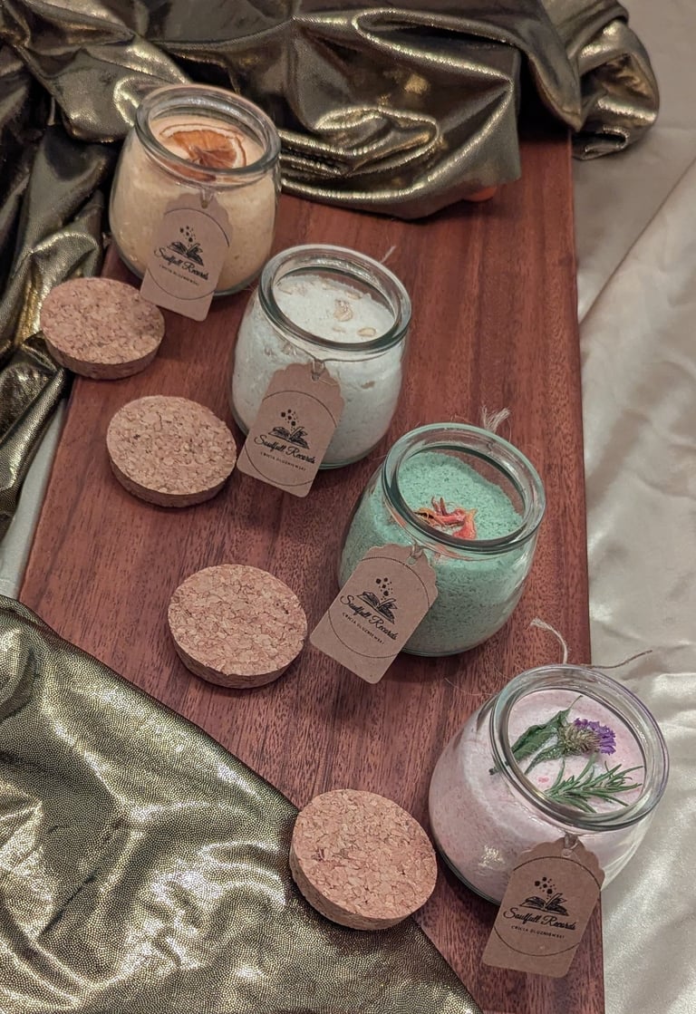 Handmade organic bath salts in glass jars with cork lids and tags on a wooden board.