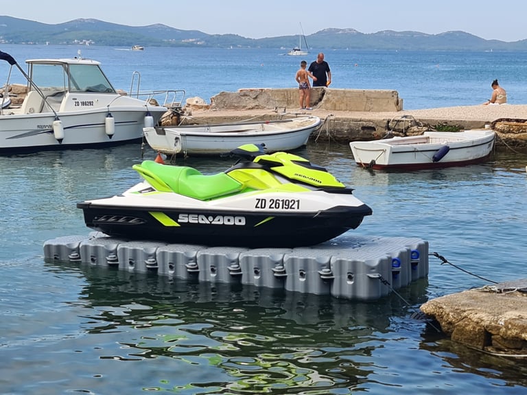 A lime green Sea-Doo jet ski parked on a floating dock in a sunny Mediterranean harbor.