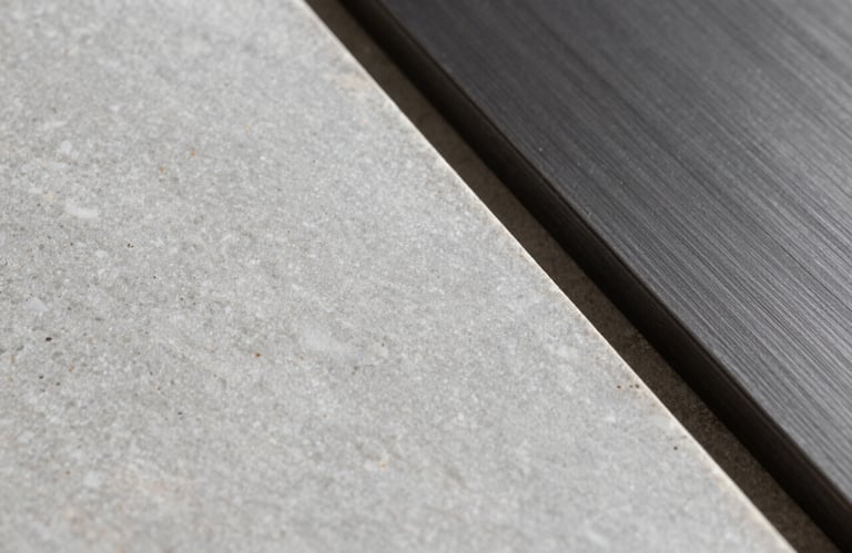 Detail shot of luxury materials: a sample of light grey travertine stone next to a piece of dark charcoal brushed metal. Soft, diffused studio lighting.