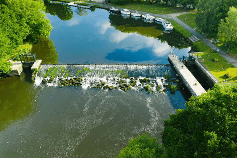 Vue aérienne d'un barrage et d'une cascade, avec des péniches amarrées et des arbres verdoyants.