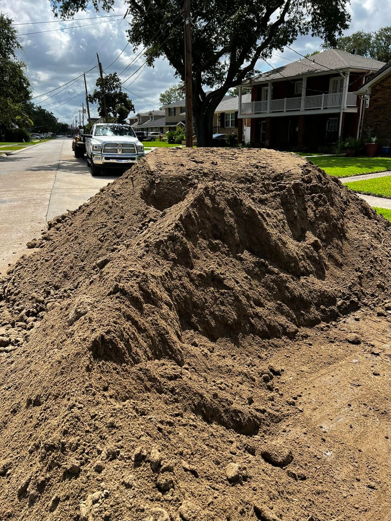 Large pile of brown landscaping topsoil delivered on a suburban driveway for ground leveling.