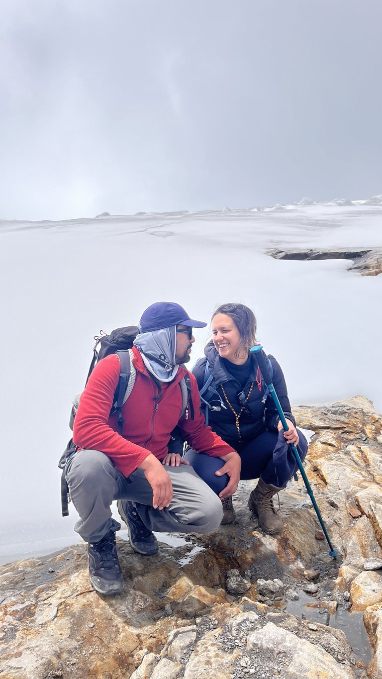 A smiling couple hiking on a snowy mountain ridge with professional trekking gear and poles.