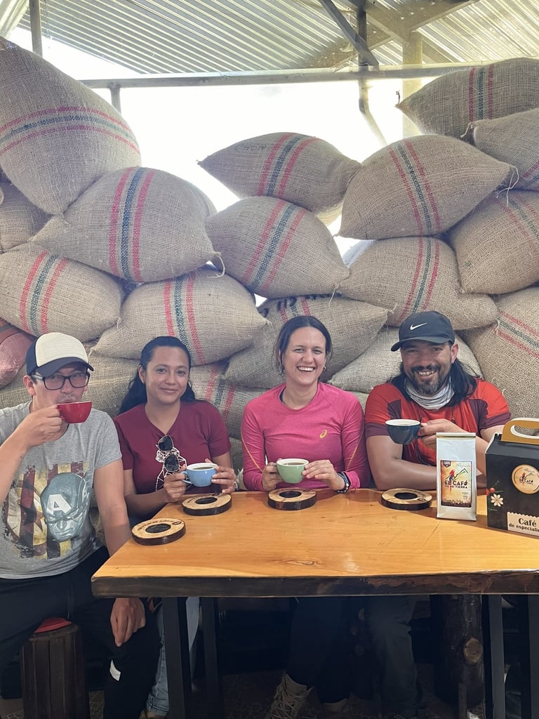 Friends tasting local coffee at a wooden table in front of burlap sacks of fresh coffee beans.