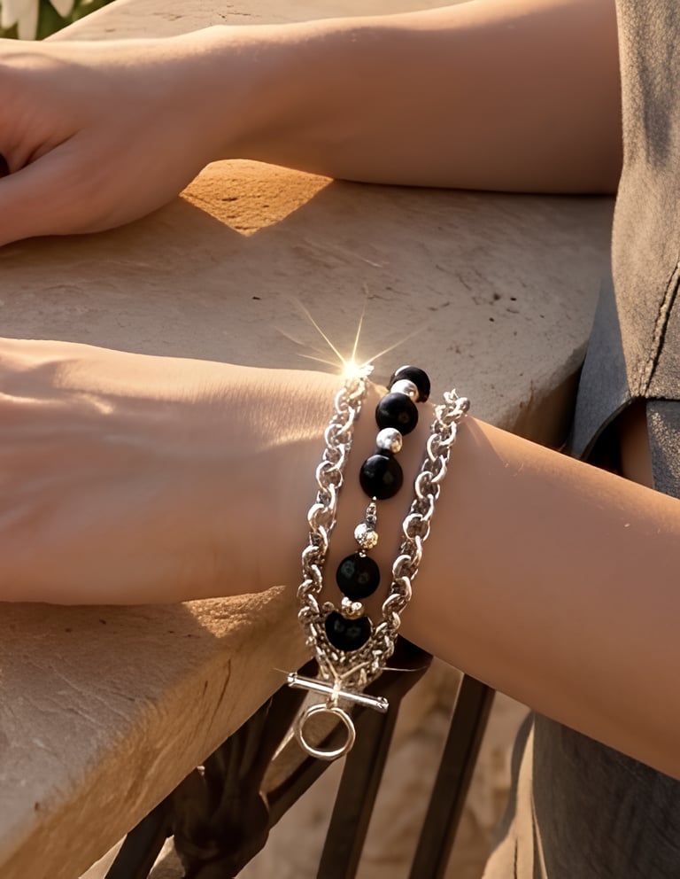 Elegant layered silver chain bracelet with black onyx beads worn on a woman's wrist at sunset.