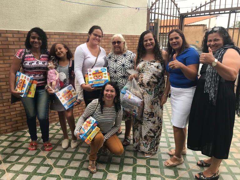 A group of women and children smiling while holding donated toys and games at a community charity event.