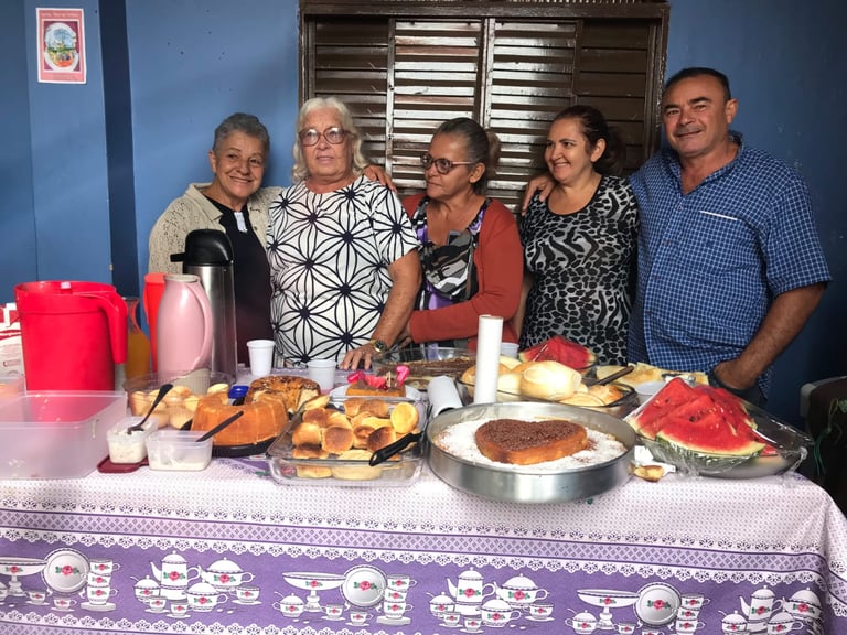 A group of happy friends gathered around a breakfast table filled with homemade cakes and fresh fruit.