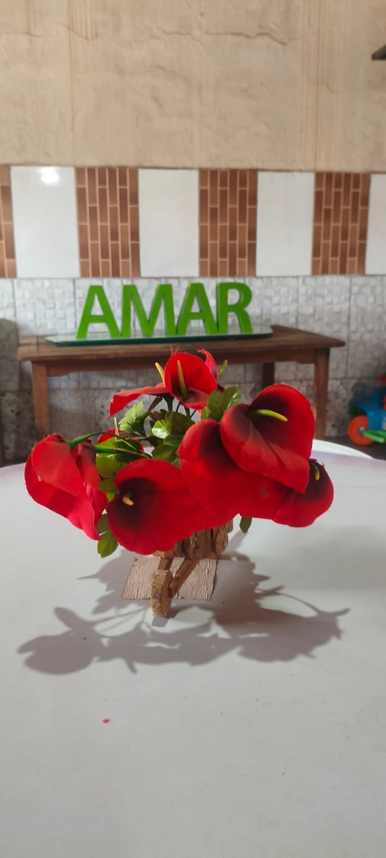 Red calla lily artificial flower arrangement on a white table with a green AMAR sign background.