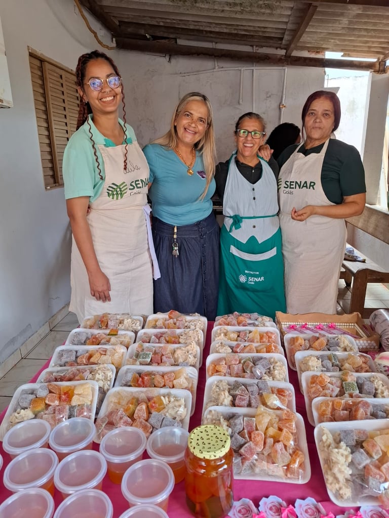 Four women smiling behind a table filled with trays of homemade fruit preserves and sweets from SENAR Goiás.
