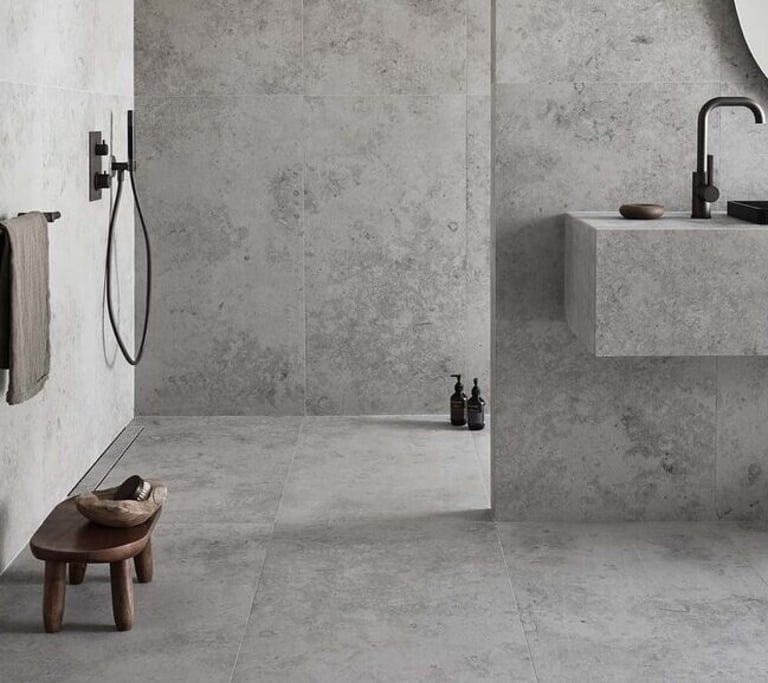 Modern minimalist bathroom featuring grey stone-effect tiles on walls and floors with black matte fixtures.