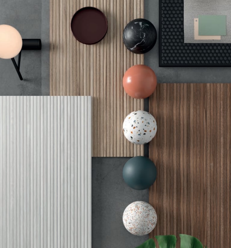 Flat lay of interior design samples featuring wood slat panels, marble spheres, and terrazzo textures.
