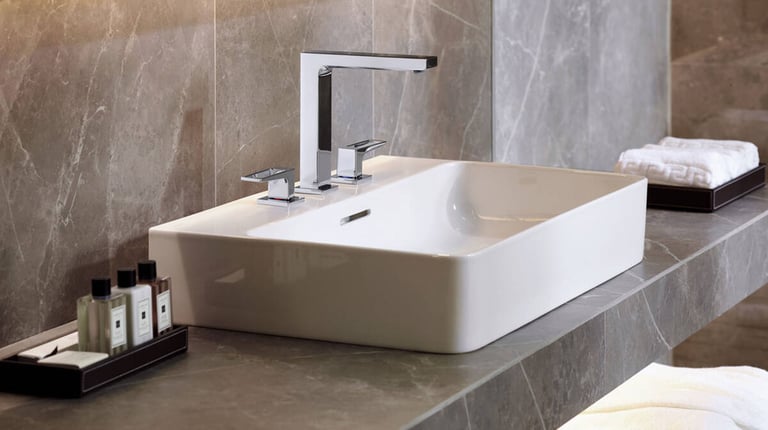 Modern white vessel sink with a chrome three-piece faucet on a grey marble bathroom vanity.