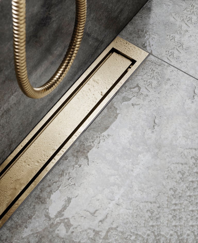 Modern brushed gold linear shower drain installed in a gray stone tile walk-in shower.