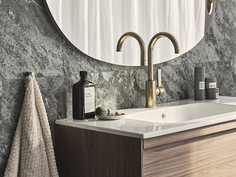 Modern bathroom vanity with a gold faucet, white sink, and grey marble tile backsplash.