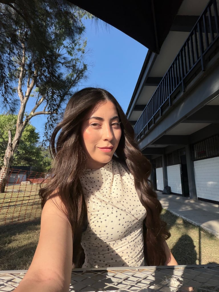 Mujer joven con cabello largo ondulado, castaño que viste un top de lunares al aire libre bajo la lu