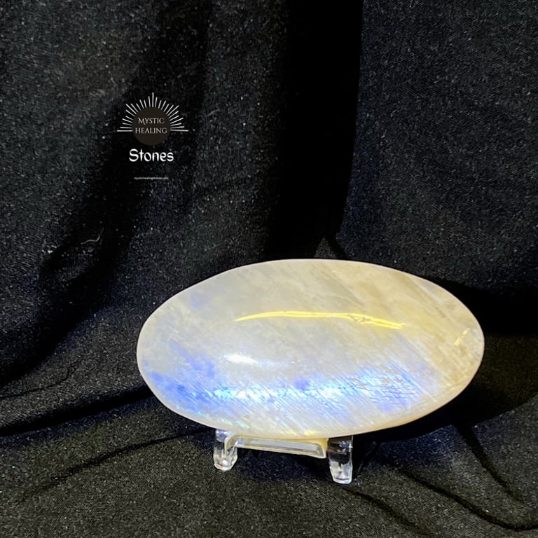 Polished moonstone palm stone with blue flash on a display stand against a black background.