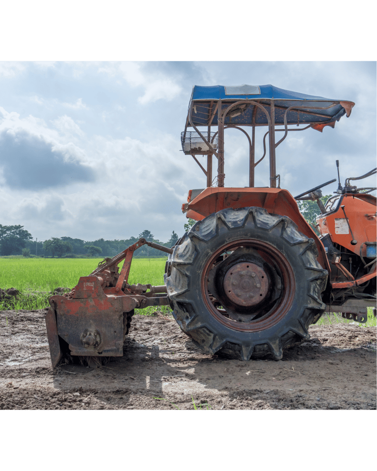 Orange agricultural campact tractor with a rotary tiller attachment parked in a muddy farm field.