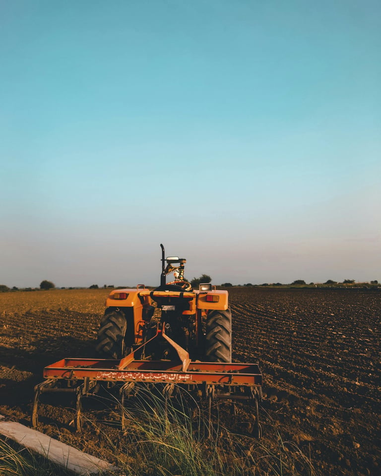 An orange farm tractor with a plow attachment stands in a tilled field under a clear blue sky.