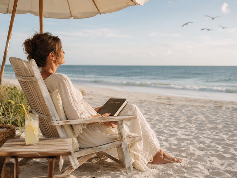 A woman relaxing on a beach chair under an umbrella reading the Holy Bible by the ocean.