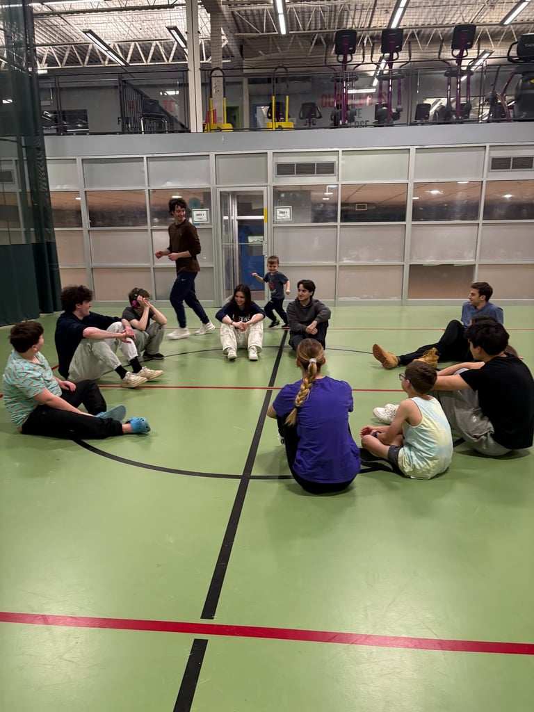 A group of children and volunteers sit to play an inclusive youth activity in a Kingston gymnasium