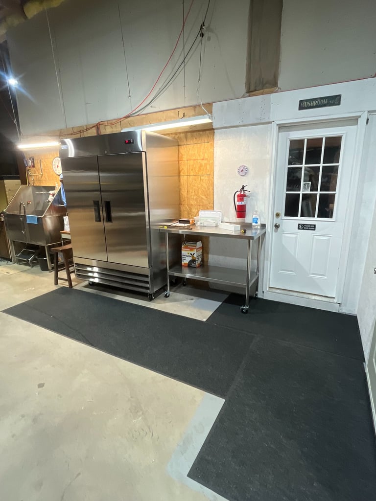 Industrial kitchen setting with a large stainless steel refrigerator and prep table next to a white door.