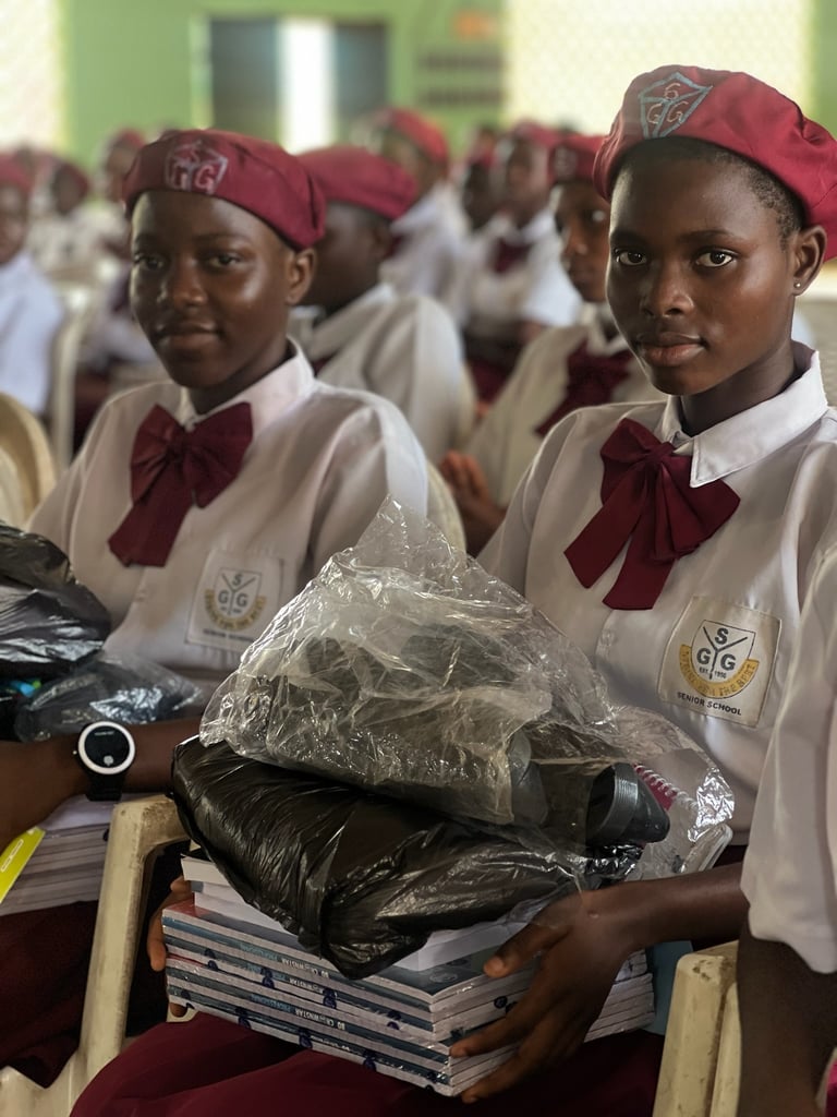 Students in red berets and white school uniforms holding educational supplies and books.