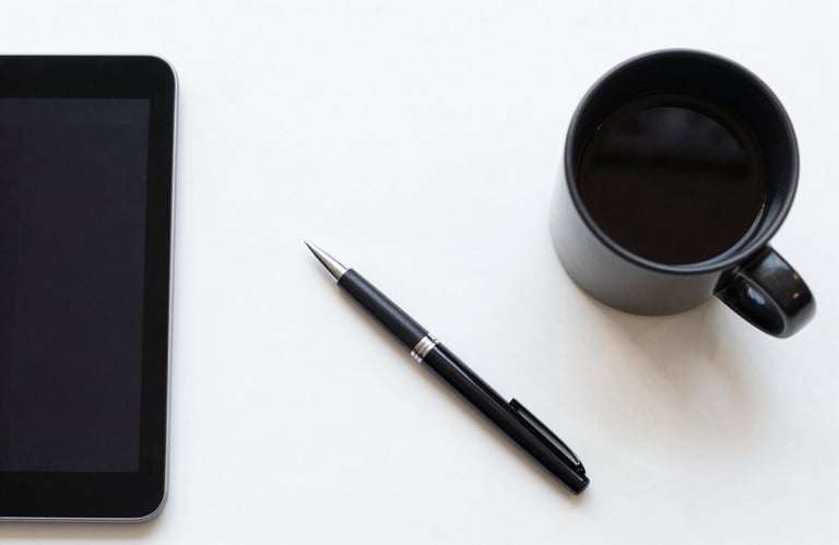 A top-down view of a designer's desk with a black coffee mug, a sleek tablet, and a professional digital pen on a white surface. The composition is clean, balanced, and symbolizes innovative digital strategy.