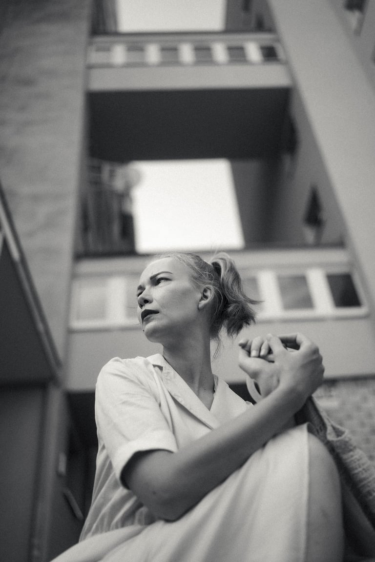 Black and white portrait of a woman looking away against a backdrop of urban architecture.
