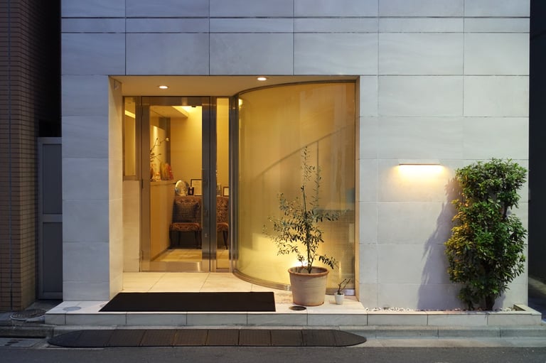 Modern storefront with a glass door, curved window, and warm lighting on a white tiled wall.