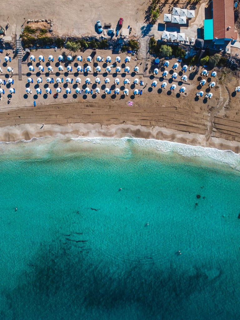 Aerial view of a tropical beach resort with rows of white umbrellas and turquoise ocean water.