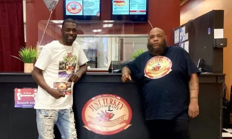Two men standing at the counter of The Original Just Turkey Restaurant in front of digital menus.